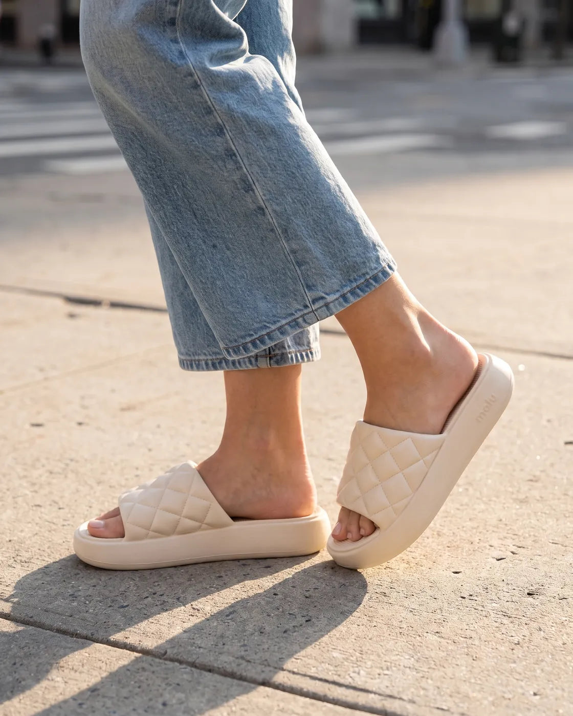 Pessoa de calça jeans andando na calçada com o chinelo molu Luxo bege